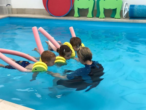 A swimming teacher supporting a small group of children in the pool