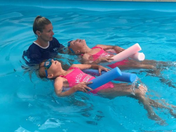 A teacher helping two children practise floating with swimming noodles