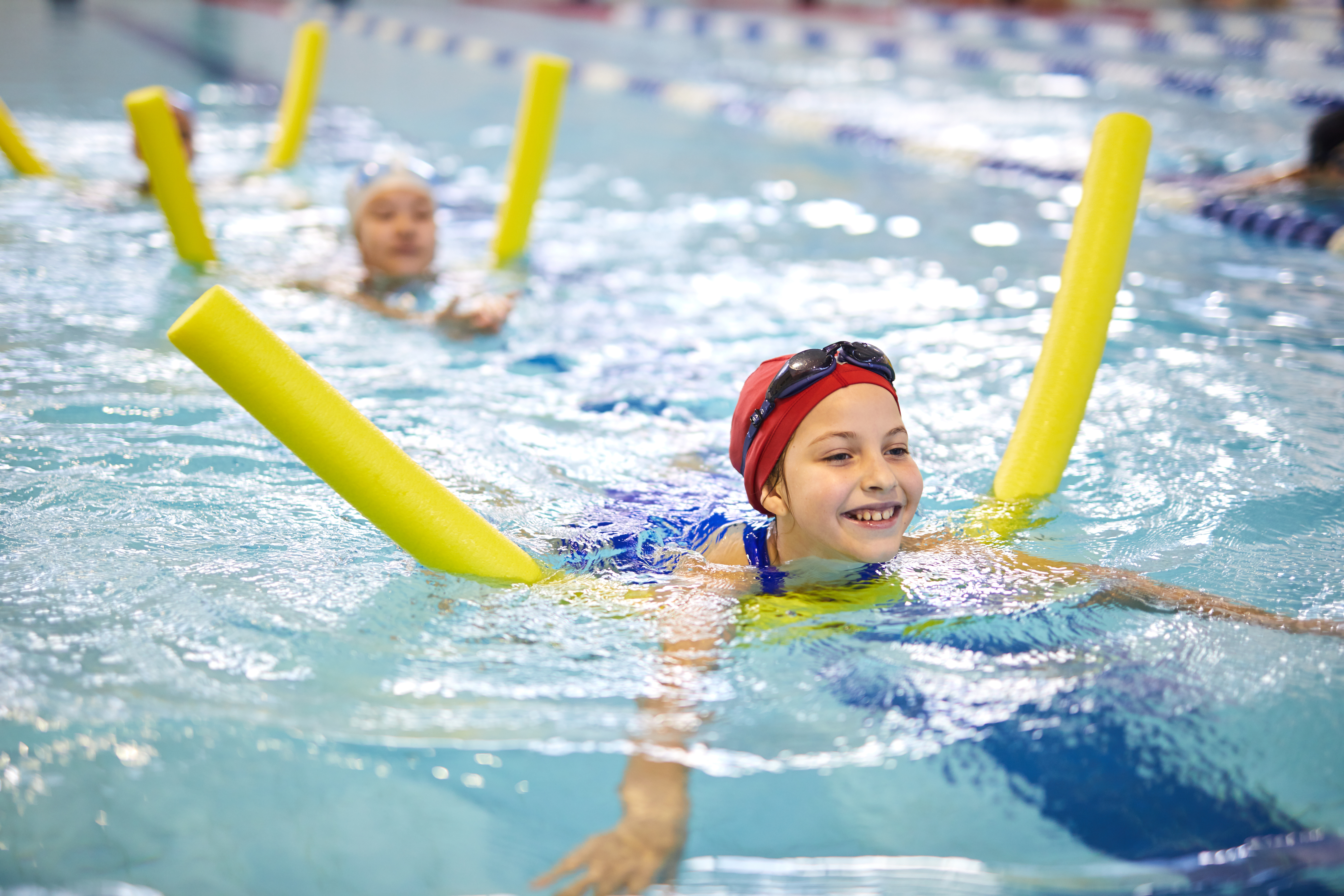 A smiling young swimmer with a yellow swimming noodle