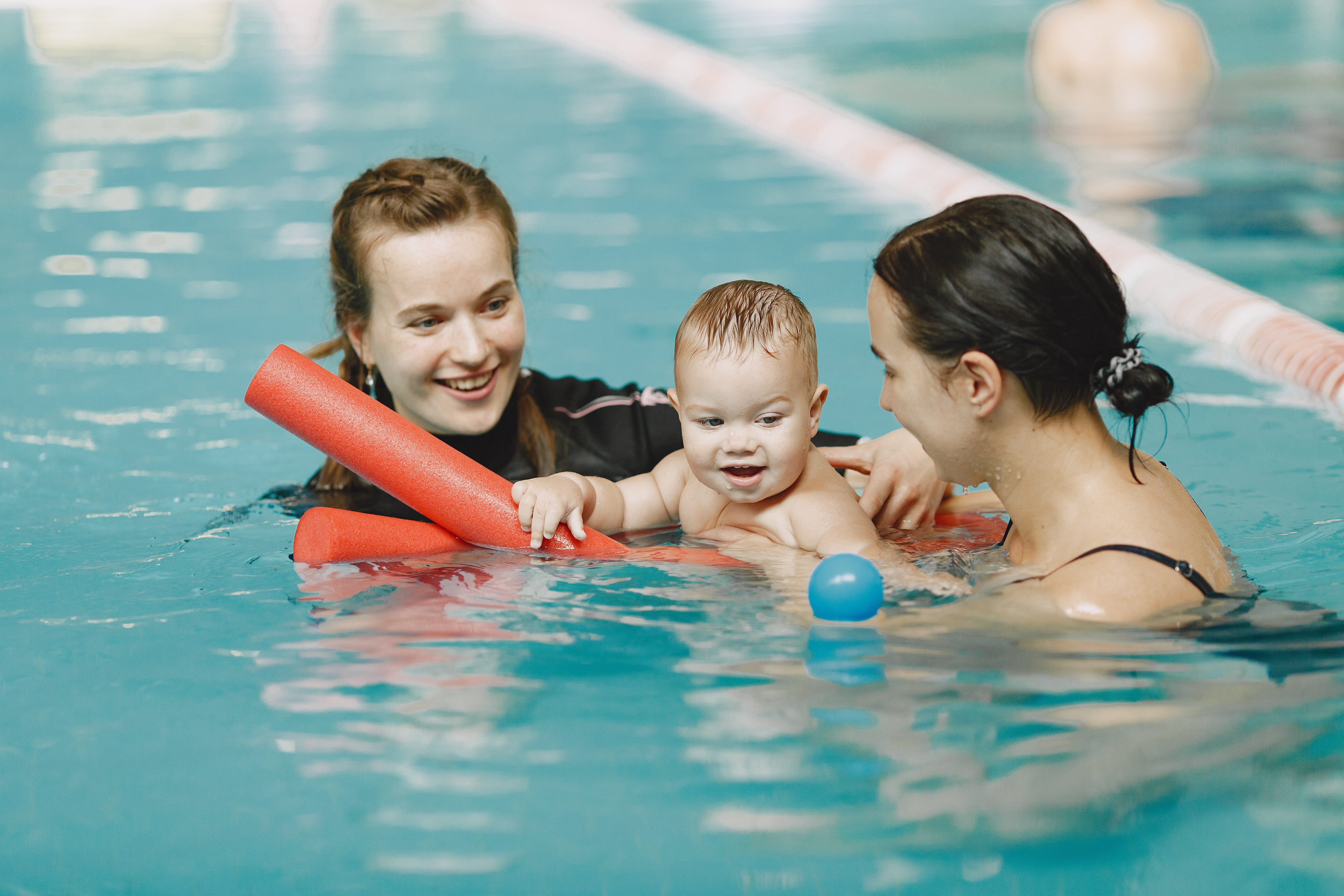 A parent supporting their baby in the swimming pool with a swimming teacher